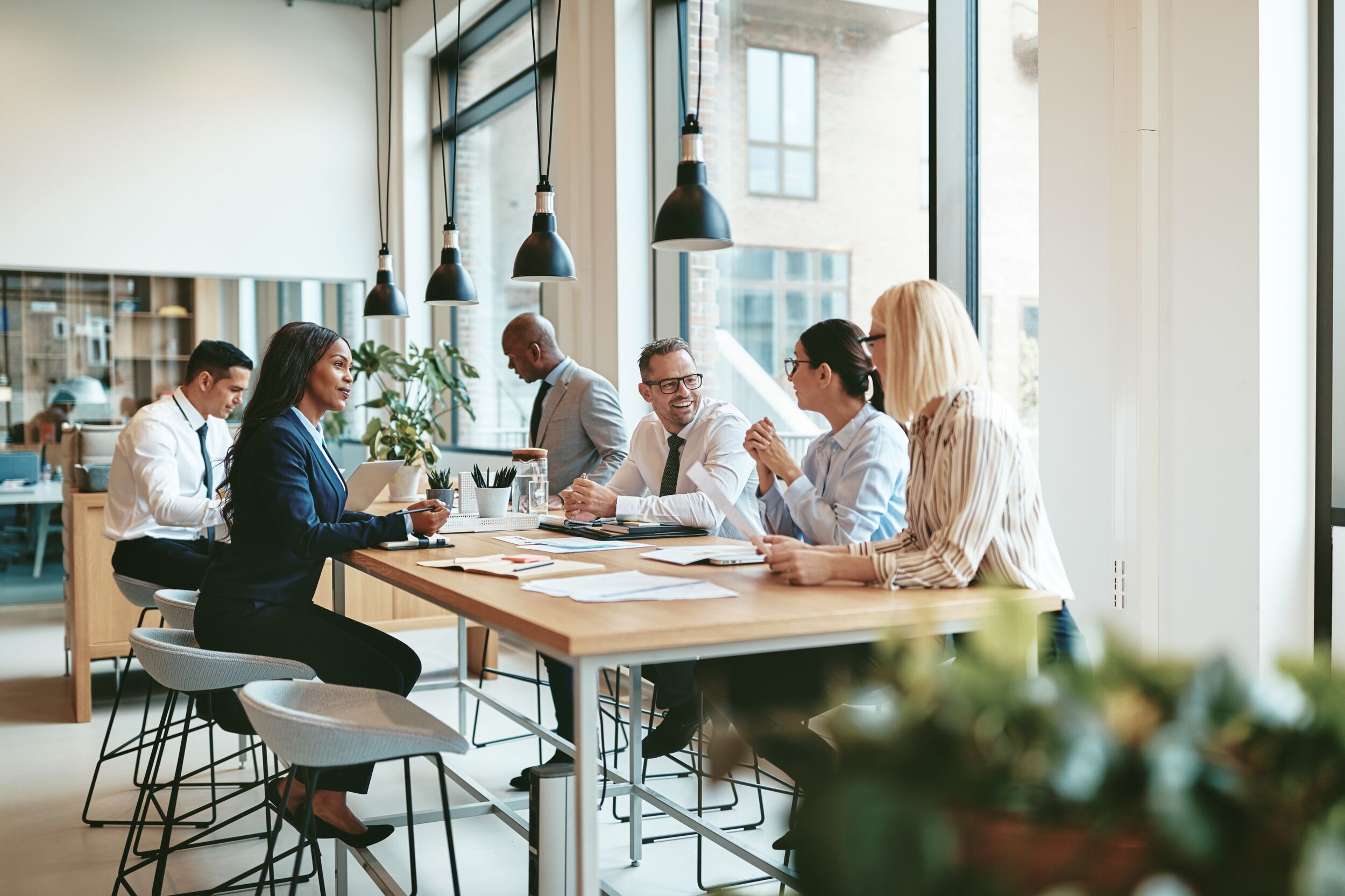 Smiling group of diverse businesspeople discussing paperwork together while having a meeting around a table in a modern office