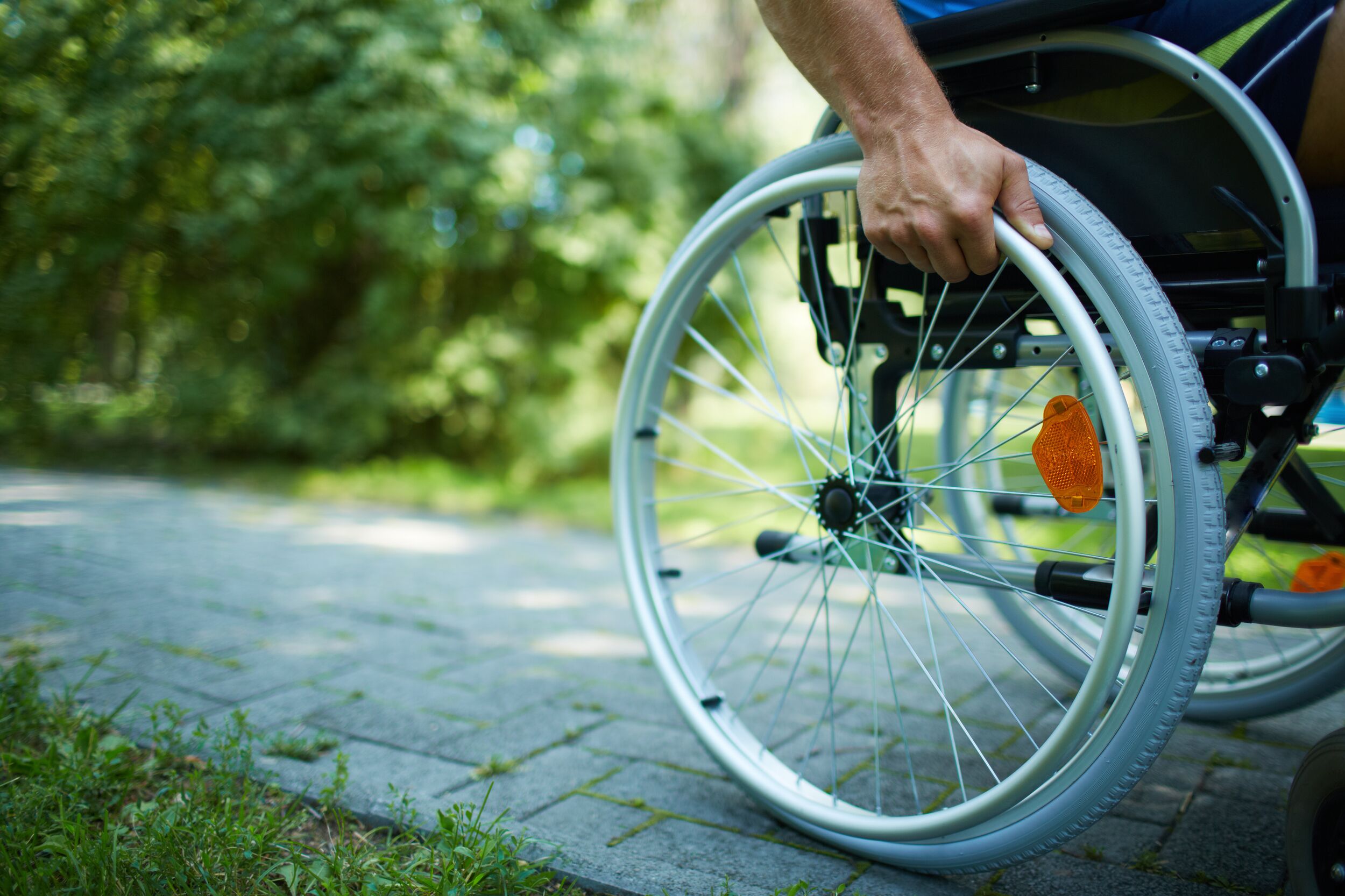 Close-up of male hand on wheel of wheelchair during walk in park
